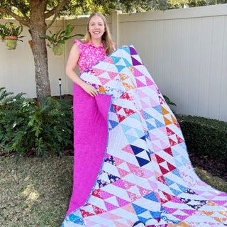 Kinetic Quilt Pattern (Download) by Homemade Emily Jane, colorful modern geometric quilt with dynamic triangular shapes displayed outdoors by a smiling maker
