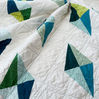 Luminary Quilt Pattern (Download) by Homemade Emily Jane featuring a white quilt with bold teal green and blue geometric shapes and stitched linework