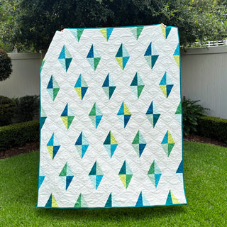 Luminary Quilt Pattern (Download) by Homemade Emily Jane featuring colorful geometric diamond shapes on a white background displayed outdoors