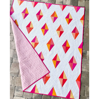 Luminary Quilt Pattern (Download) by Homemade Emily Jane, a modern quilt with colorful geometric diamond shapes on a white background and pink backing