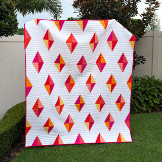 Luminary Quilt Pattern (Download) by Homemade Emily Jane, a modern geometric quilt with vibrant pink, orange, and yellow diamond shapes on white fabric