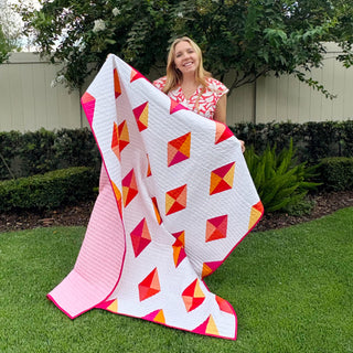 Luminary Quilt Pattern (Download) by Homemade Emily Jane featuring a modern geometric quilt with pink white red and orange diamond shapes displayed outdoors
