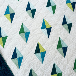 Luminary Quilt Pattern (Download) by Homemade Emily Jane featuring a modern white quilt with colorful geometric diamond shapes and intricate quilting lines