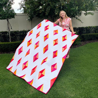 Luminary Quilt Pattern (Download) by Homemade Emily Jane, colorful modern geometric quilt with bright pink, orange, and yellow shapes displayed outdoors
