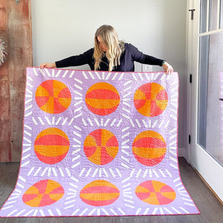Nothin' But Net Quilt Pattern (Download) by Jessica Steele Design featuring a purple quilt with oversized orange and pink basketball blocks and striped sashing