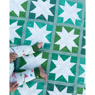 Keepsake Quilt Pattern (Download) by Homemade Emily Jane showing a green and teal sawtooth star quilt with a child resting on it