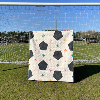 Soccer Party Quilt Pattern (Download) by Jessica Steele Design showing a modern soccer ball quilt displayed in front of a soccer goal on a sunny field