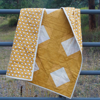 Solitaire Quilt Pattern (Download) by Homemade Emily Jane featuring a mustard yellow modern geometric quilt with white accents draped over a metal railing